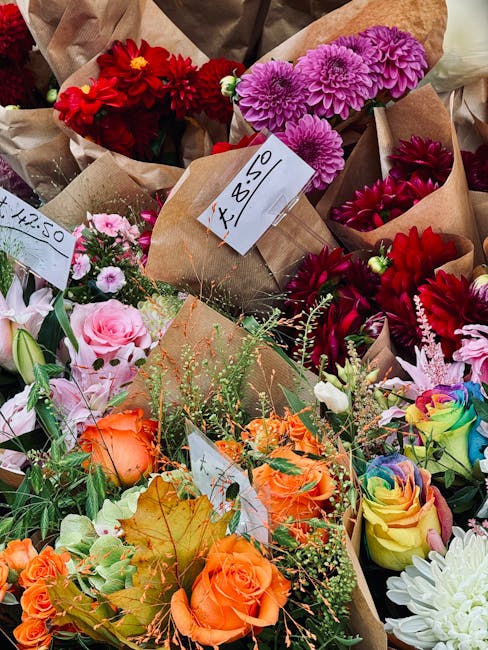 A vibrant display of fresh floral arrangements featuring a variety of flowers including deep red dahlias, bright pink dahlias, soft pink roses, orange roses, and multicoloured roses with rainbow hues.