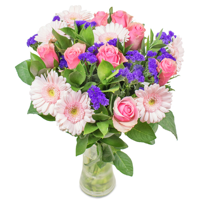 An exuberant bouquet arranged by Creekmouth Florist showcases a sophisticated interplay of roses and gerbera daisies-each stem carefully chosen for peak freshness and visual harmony. Around 7-9 medium pink roses, many just at the cusp of full bloom, display tightly coiled petals and classic spirals, their colour reminiscent of blossoms seen near Barking Riverside in early spring. Interspersed throughout are 5-7 pale pink gerberas, their wide, ruffled petals and creamy centres shining in soft daylight. Bright purple statice, with its papery clusters, adds a playful texture, drawing the eye and introducing a deeper tone that balances the lighter hues. The arrangement is set against a base of glossy, deep green foliage, the leaves fresh and abundant, grounding the composition with their vibrant, lively appearance-an echo of Creekmouth's green spaces. Stems rest in a clear glass vase, visible through transparent water, completing the natural, polished effect. The bouquet, ideal for local deliveries from Creekmouth Florist, embodies the area's love for understated beauty and is thoughtfully suited for celebrations, special occasions, or as a heartfelt gift across the community.